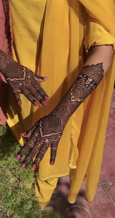 a woman with henna tattoos on her hands and arms, standing in front of some grass