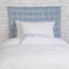 a bed with white pillows and blue headboard against a brick wall in a bedroom