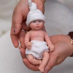 a person holding a baby doll in their hands, wearing a white hat and diaper