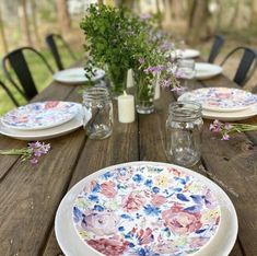 a wooden table topped with plates and vases filled with flowers