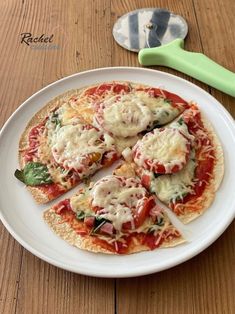 a small pizza on a white plate next to a green spatula