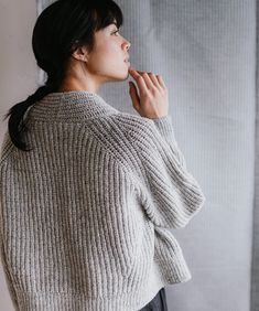 a woman standing in front of a window wearing a sweater