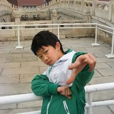 a young boy standing on top of a white fence next to a building with a clock tower in the background