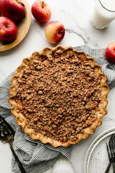 an apple pie is sitting on a table next to some plates and bowls with apples