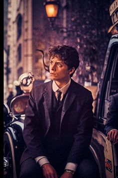 a man in a suit and tie sitting on the back of a car next to a lamp post