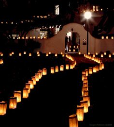 many lit up paper lanterns are in the dark, with one person standing at the end