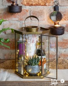 a small lantern with succulents and candles in it on a table next to a brick wall