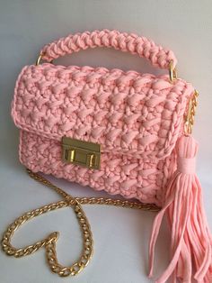 a pink crocheted purse with a gold chain and tasselled handle, on a white background