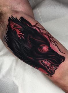 a man's arm with a black and red tattoo design on it, featuring a wolf