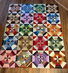 a multicolored quilt is laying on the floor in front of a wooden floor