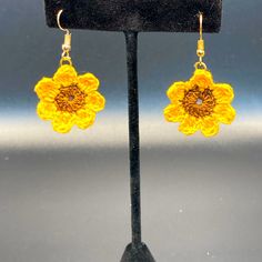 a pair of yellow flower earrings on a black display stand in front of a gray background