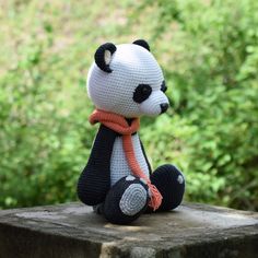 a crocheted panda bear sitting on top of a cement block in front of some bushes