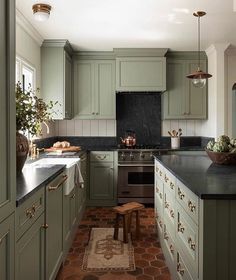 a kitchen with green cabinets and black counter tops, along with an area rug on the floor