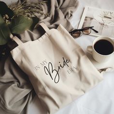 a tote bag sitting on top of a bed next to a cup of coffee