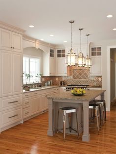 a large kitchen with wooden floors and white cabinets on the walls, along with an island in the middle