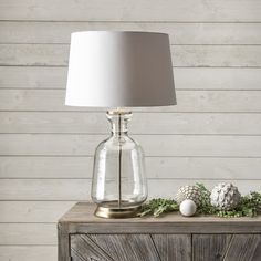 a table lamp sitting on top of a wooden cabinet next to a white ball and pine cone