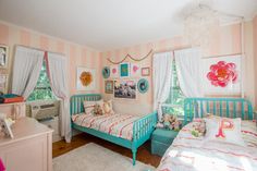 two twin beds in a pink and white striped room with pictures on the wall above them