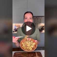 a woman is holding a plate with food in it and smiling at the camera while standing next to a cutting board