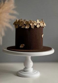 a chocolate cake with gold leaf decorations on top is sitting on a white pedestal next to a feather