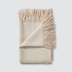 a white blanket with fringes on the top and bottom, folded in two different colors