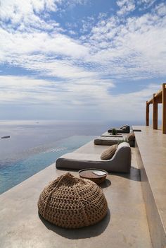 some lounge chairs sitting on the edge of a swimming pool with an ocean in the background