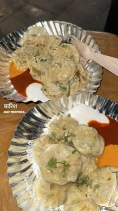 two silver plates filled with dumplings covered in gravy on top of a wooden table