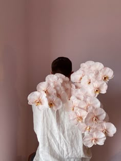 a man with flowers on his back standing in front of a pink wall and looking down at the ground