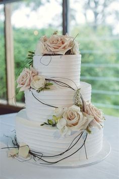 a three tiered cake with flowers on it sitting on top of a white table