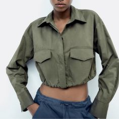 Collared Shirt With Long Sleeves And Pleated Cuffs. Front Patch Pockets With Flaps. Darted Detail On The Back. Elastic Hem. Button-Up Front Hidden By A Placket. Light Khaki Khaki Long Sleeve Utility Top, Green Long Sleeve Cropped Jacket For Fall, Cropped Winter Utility Jacket With Pockets, Winter Cropped Utility Jacket With Pockets, Winter Cropped Tops With Pockets, Green Long Sleeve Cropped Jacket With Pockets, Solid Utility Tops For Fall, Green Cropped Jacket With Pockets, Utility Solid Color Tops For Fall