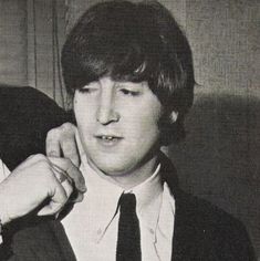 the young man is adjusting his tie in black and white photo, with one hand on another's shoulder