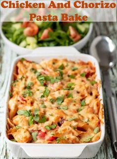 a casserole dish filled with pasta, cheese and vegetables next to a salad