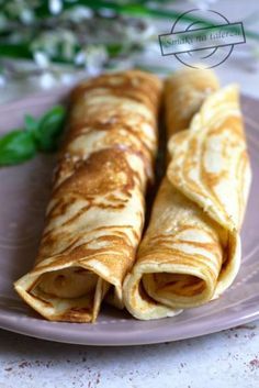 two crepes sitting on top of a purple plate next to green leaves and flowers