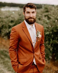 a man with a beard wearing an orange suit and flower in his lapel is posing for the camera