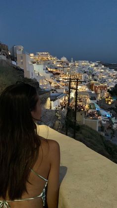 a woman sitting on top of a balcony next to the ocean at night with city lights in the background