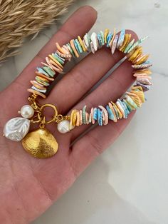 a hand is holding a bracelet with shells and charms on it's sides, along with a gold charm