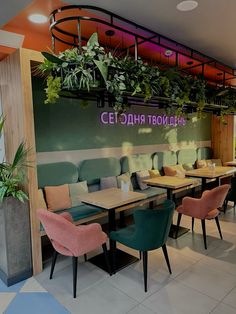 an empty restaurant with green plants hanging from the ceiling and pink chairs on the tables