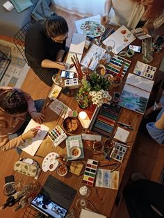 three people are sitting at a table with art supplies and paintbrushes on it