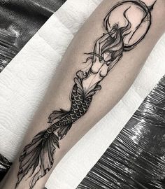 a black and white photo of a mermaid tattoo on the right arm with a half moon above it