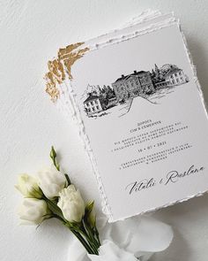 a white and gold wedding stationery with flowers on the side, next to it