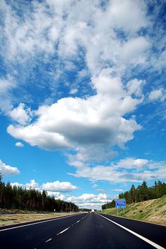 an empty highway with blue sky and white clouds