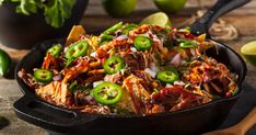 a skillet filled with taco salad and tortilla chips next to limes