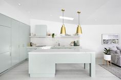 a white kitchen with gold pendant lights hanging from the ceiling