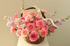 a basket filled with lots of pink flowers on top of a white table next to a wall