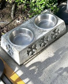 two metal bowls sitting on top of a cement block