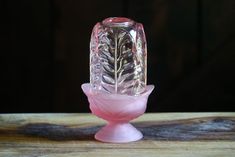 a pink glass vase sitting on top of a wooden table next to a black wall