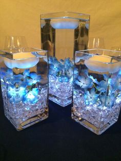 three clear vases filled with water and blue flowers on top of a black table