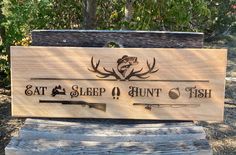 a wooden sign that says eat sleep hunt fish on the side of a bench in front of trees