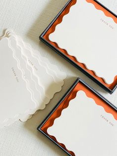 three stationery cards with scalloped edges on a white tablecloth, one in orange and the other in black