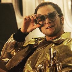 a man in gold jacket and sunglasses talking on cell phone