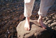 a person standing on top of a rock in the water with their bare feet sticking out